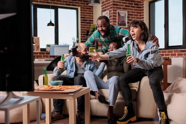 Groupe diversifié d'amis célébrant la victoire des jeux vidéo, se sentant heureux de gagner un jeu de compétition avec des lunettes vr. Profiter de la victoire du jeu et boire de la bière dans des bouteilles, une fête amusante.