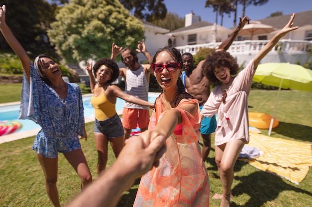 Groupe diversifié d'amis heureux s'amusant à danser lors d'une fête à la piscine. traîner et poser pour la caméra à l'extérieur en été.