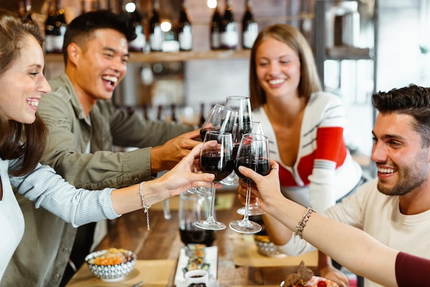 Groupe diversifié d'amis multiculturels célébrant ensemble au restaurant en riant et en plaisantant en portant un toast avec des verres de vin rouge