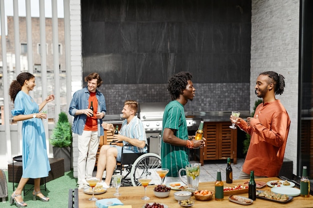 Photo groupe diversifié d'amis profitant d'une fête sur une terrasse extérieure et communiquant y compris une personne à l'heure