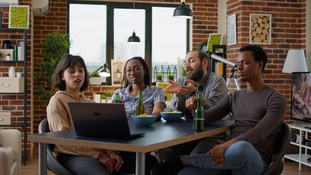 Groupe diversifié d'amis regardant des vidéos Internet sur un ordinateur portable, utilisant le réseau de médias sociaux en ligne pour s'amuser ensemble. Jeunes profitant d'une réunion moderne avec spectacle en direct sur ordinateur.