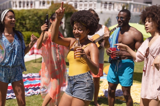 Groupe diversifié d'amis s'amusant et dansant lors d'une fête à la piscine. traîner avec des boissons et danser sur la pelouse du jardin en été.