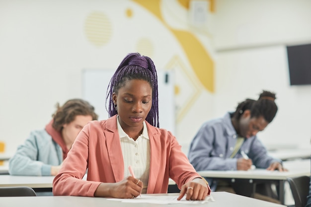 Groupe diversifié d'étudiants étudiant en classe en mettant l'accent sur une jeune femme afro-américaine assise au bureau devant, espace pour copie