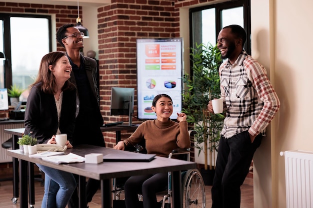 Photo groupe diversifié de personnes s'amusant sur le lieu de travail pendant la pause, riant et appréciant la conversation avec un employé paralysé. femme vivant avec un handicap physique chronique en fauteuil roulant au travail.