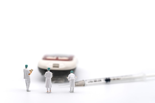 Groupe de docteur miniature figure avec dossier patient debout avec glucomètre et seringue à insuline sur fond blanc. Utilisation comme concept de diabète, de glycémie, de soins de santé et de personnes.