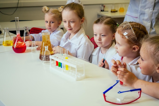 groupe d'écolières avec enseignant dans un laboratoire scolaire faisant une expérience observant la réaction chimique avec le colorant avec du vinaigre et du volcan de soude portant une robe blanche en verre uniforme