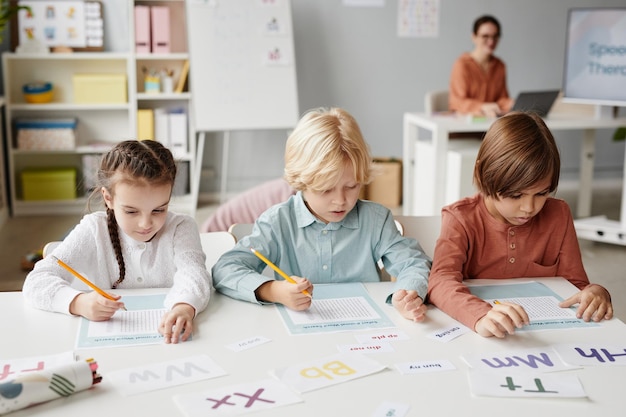 Groupe d'écoliers assis à la table et prenant des notes sur des papiers pendant la leçon à l'école avec...