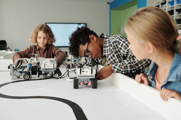 Groupe d'écoliers interculturels mignons jouant avec des robots jouets faits à la main