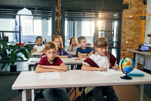 Groupe d'élèves de l'école primaire assis aux bureaux et passer l'examen en classe de l'école intelligente moderne.