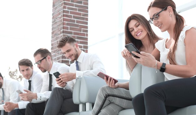 Groupe d'employés avec des gadgets assis dans la salle d'attente du bureau