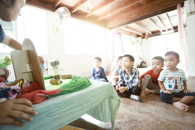 Un groupe d'enfants asiatiques s'assoit et écoute l'enseignant raconter une histoire avec des poupées Waldorf fabriquées à la main.