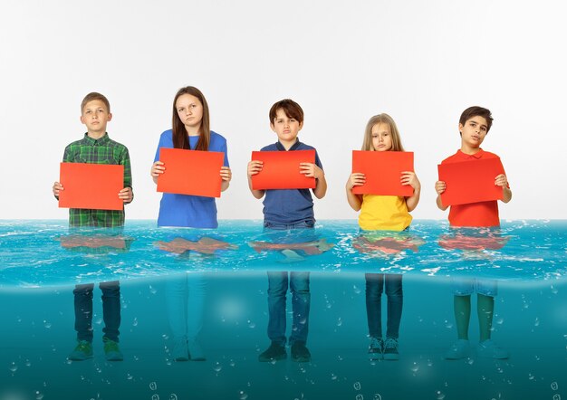 Groupe d'enfants avec des bannières rouges vierges debout dans l'eau de la fonte des glaciers, réchauffement climatique