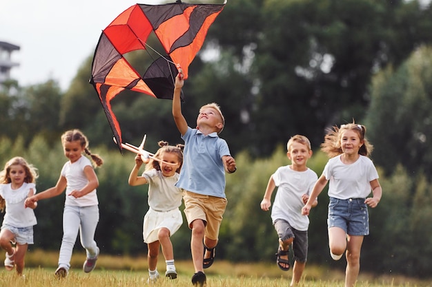 Un groupe d'enfants courent et jouent avec un cerf-volant sur un champ vert.