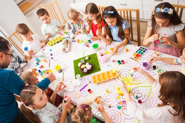 Groupe d'enfants avec un enseignant peignant des oeufs de Pâques à la table dans la salle de classe