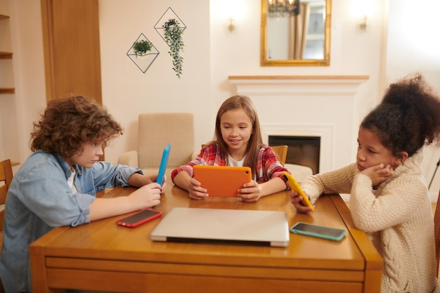 Un groupe d'enfants avec des gadgets en mains assis à la table