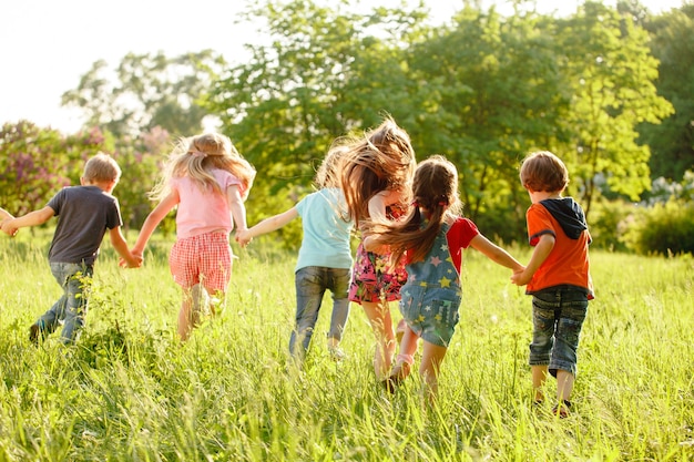 Un groupe d'enfants heureux, garçons et filles, courant dans le parc sur l'herbe par une journée d'été ensoleillée.