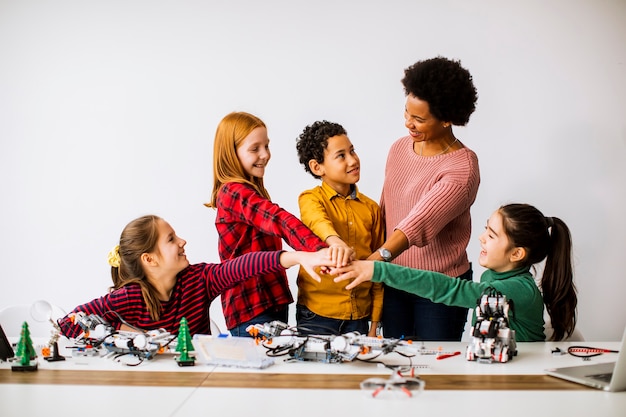 Groupe d'enfants heureux avec leur professeur de sciences afro-américaines programmant des jouets électriques et des robots en classe de robotique