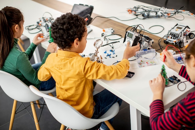 Groupe d'enfants heureux de programmer des jouets électriques et des robots en classe de robotique