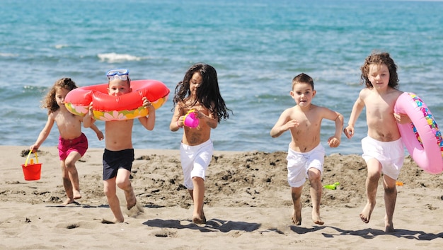 groupe d'enfants heureux s'amuser sur la plage tout en jouant avec des jouets courir sauter