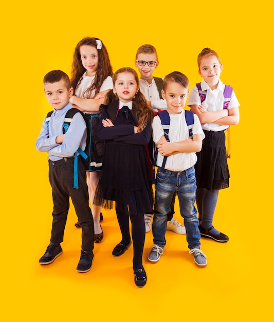 Groupe d'enfants heureux en uniforme avec des sacs d'école étreignant et regardant la caméra sur fond jaune