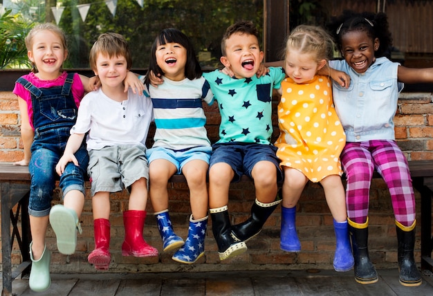 Groupe d&#39;enfants de maternelle amis bras autour assis et souriant amusant