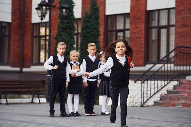 Groupe d'enfants en uniforme scolaire posant devant la caméra à l'extérieur ensemble près du bâtiment de l'éducation.