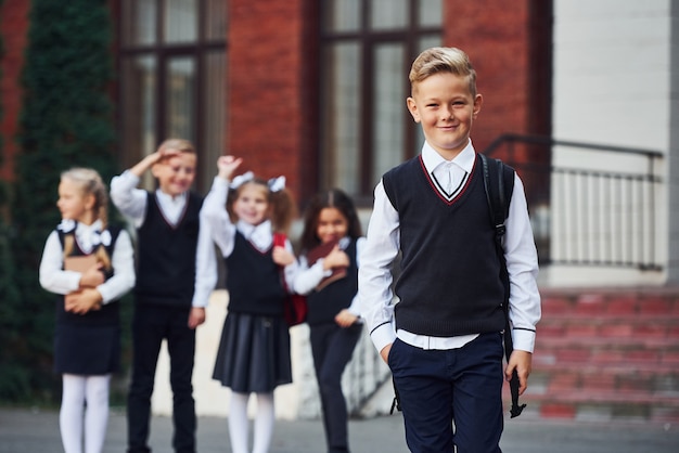 Groupe d'enfants en uniforme scolaire posant devant la caméra à l'extérieur ensemble près du bâtiment de l'éducation.