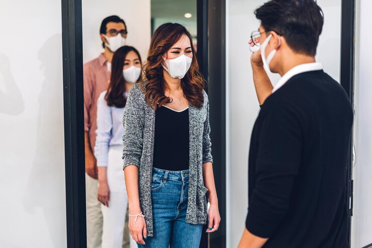 Photo groupe d'entreprises asiatiques professionnelles et utilisant un thermomètre infrarouge pour vérifier la fièvre du personnel de la température corporelle avant de travailler en quarantaine pour le coronavirus portant un masque de protection au bureau