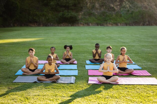 Groupe d'étudiants divers pratiquant le yoga et méditant assis sur un tapis de yoga dans le jardin à l'école