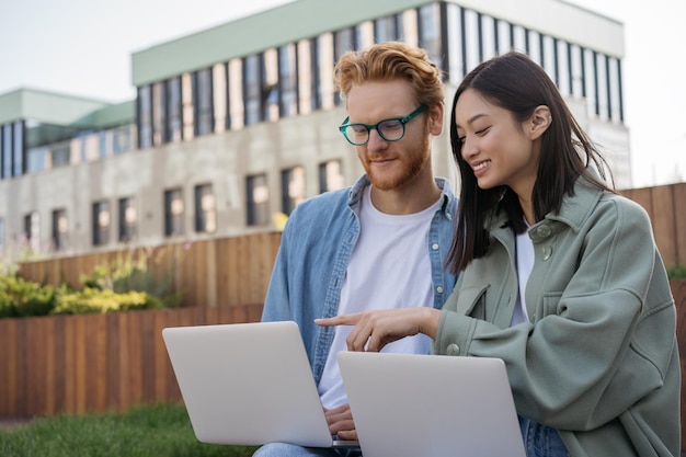 Groupe d'étudiants diversifiés souriants étudiant ensemble l'apprentissage à distance assis sur le campus universitaire