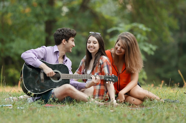 Groupe d'étudiants avec une guitare se détendre assis sur l'herbe