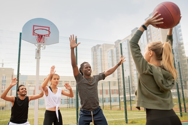 Photo groupe d'étudiants interculturels ou d'amis en tenue de sport jouant au basket-ball sur une aire de jeux en milieu urbain