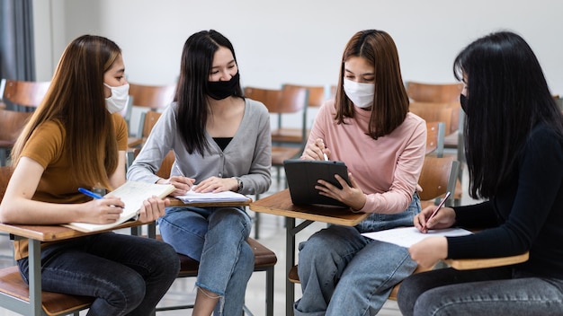 Groupe d'étudiants internationaux divers portant des masques de protection et parlant, discutant du projet, assis au bureau dans la salle de classe à l'université