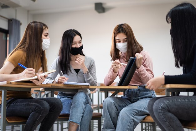 Groupe d'étudiants internationaux divers portant des masques de protection et parlant, discutant du projet, assis au bureau dans la salle de classe à l'université