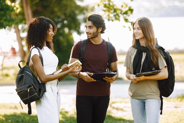 Groupe d'étudiants internationaux souriants se tenant ensemble dans un parc à l'université. Filles africaines et caucasiennes et garçon indien parlant à l'extérieur