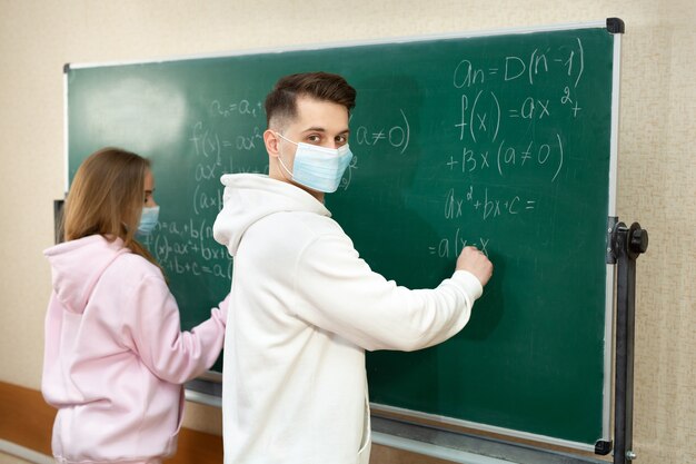 Groupe d'étudiants avec un masque facial écrivant au tableau dans la salle de classe pendant la pandémie