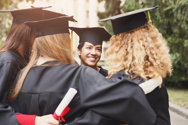 Un groupe d'étudiants multiethniques se serrant contre leur diplôme. Concept d'éducation, de qualification et de robe.