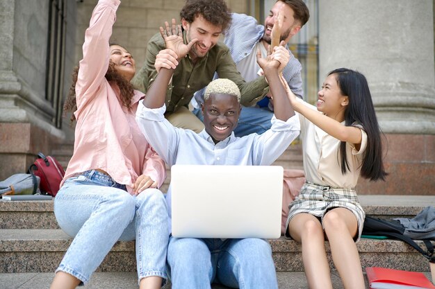 Photo groupe d'étudiants avec un ordinateur portable se donnant un high five