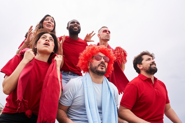 Photo groupe de fans d'une équipe de football dans les tribunes portant des chemises rouges avec un fan de l'équipe adverse