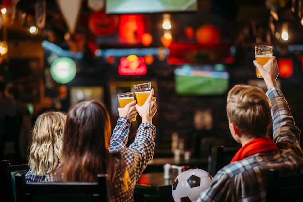 Groupe de fans de football avec foulard et balle regardant match et boit de la bière au bar des sports. Diffusion télévisée, loisirs de jeunes amis dans un pub, l'équipe favorite gagne