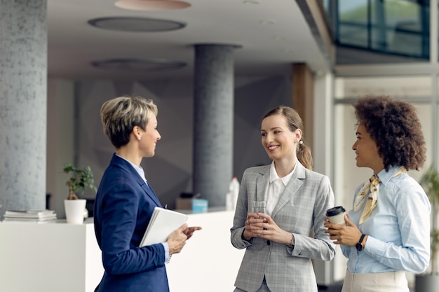 Groupe de femmes d'affaires heureuses parlant debout dans un couloir