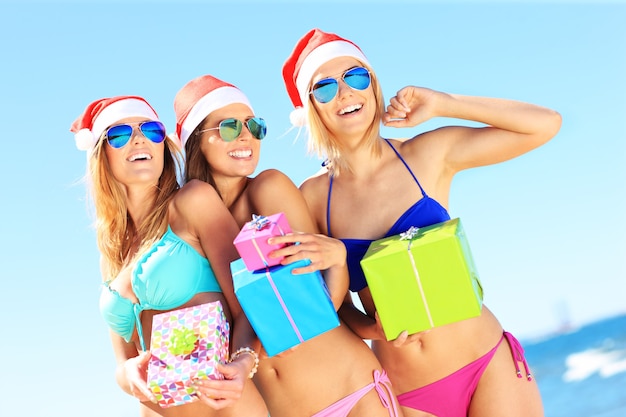 groupe de femmes en bikini et chapeaux du père Noël tenant des cadeaux sur la plage
