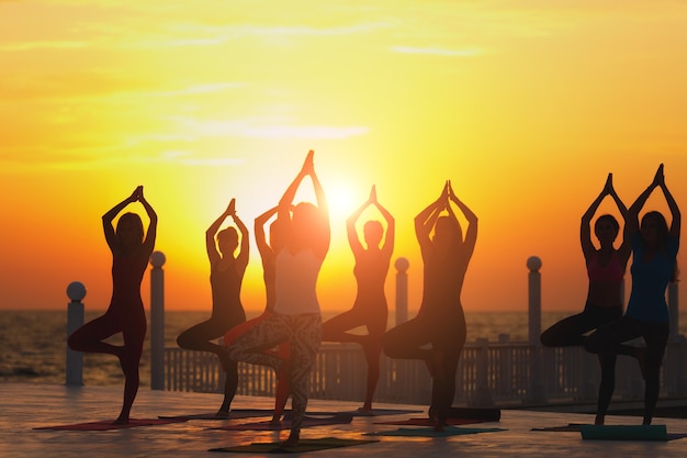 Le groupe de femmes faisant du yoga au lever du soleil près de la mer