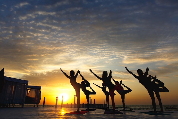 Le groupe de femmes faisant du yoga au lever du soleil près de la mer