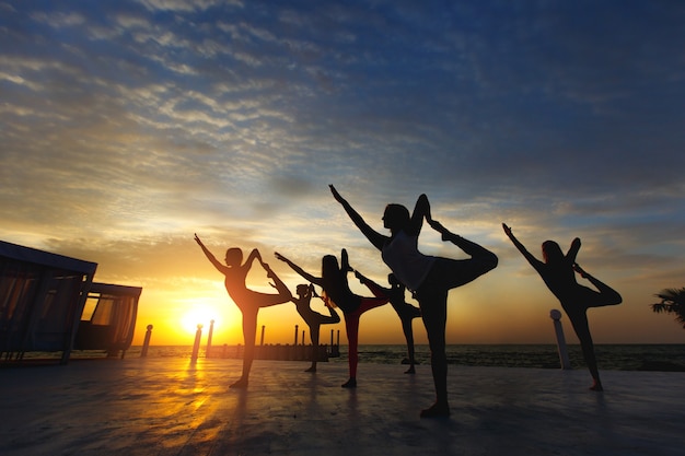 Le groupe de femmes faisant du yoga au lever du soleil près de la mer