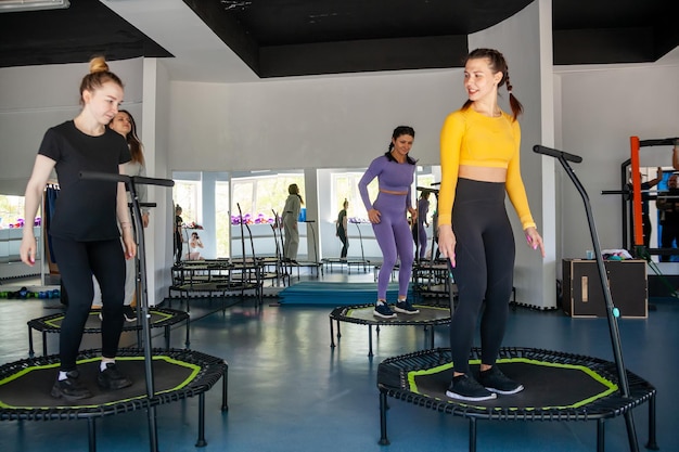 Groupe de femmes heureuses s'échauffant avant de s'entraîner en salle de sport sautant sur trampoline