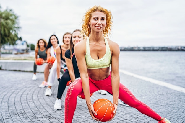 Un groupe de femmes sportives posent, effectuant des exercices avec des boules orange, dans la rue près de l'eau. Mode de vie actif
