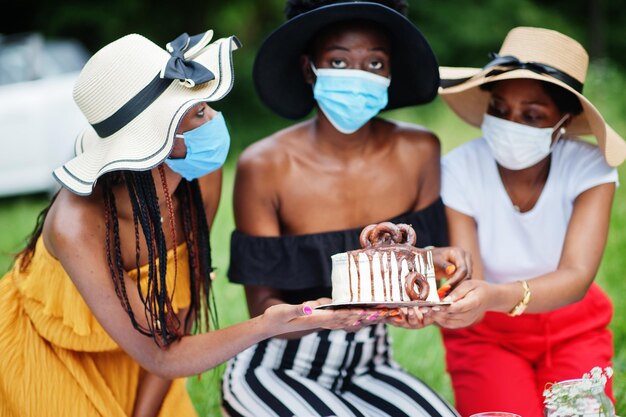 Groupe de filles afro-américaines avec des masques faciaux célébrant la fête d'anniversaire en plein air avec décor pendant la pandémie de coronavirus.