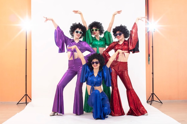 Un groupe de filles en costumes évasés colorés et perruques afro posent dans un studio photo