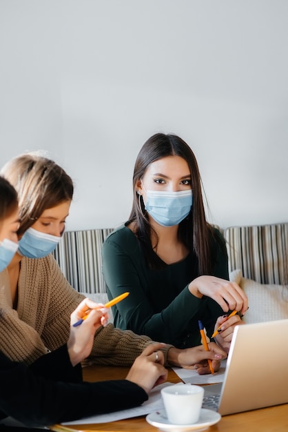 Un groupe de filles masquées est assise dans un café et travaille sur des ordinateurs portables. Enseigner aux étudiants.